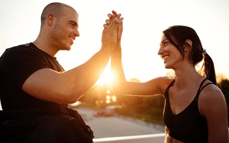 Ein Bild eines Fitnesstrainers und eines Kunden, die nach einer erfolgreichen Trainingseinheit ein High-Five feiern und Fortschritte und Erfolge feiern.